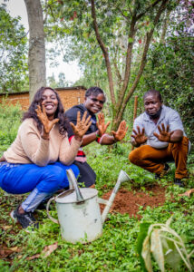 Three Kenyan people from Katakmega helping to plant a sapling tree in a forest. They are holding up their hands, which are caked in mud. after planting a sapling.